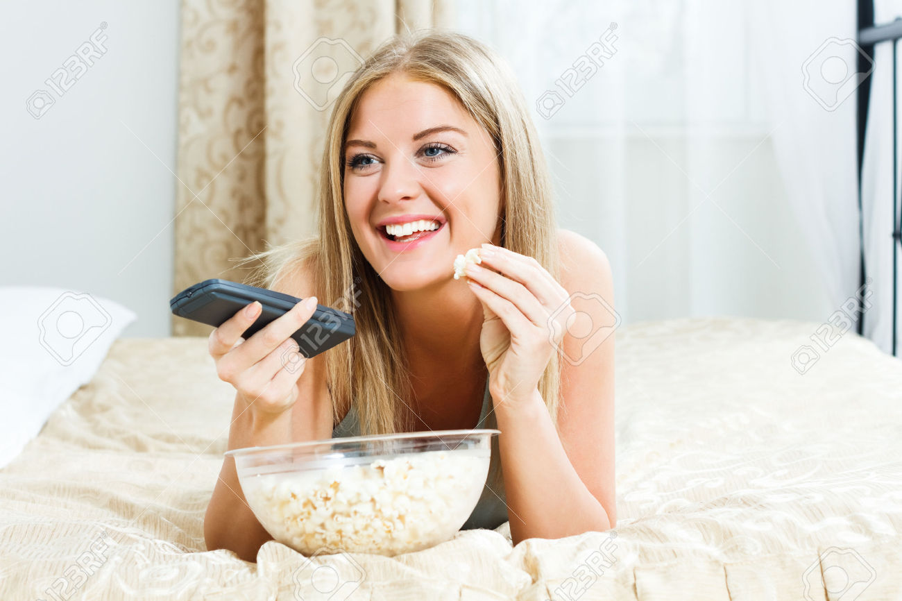 27498580-beautiful-blonde-woman-lying-on-her-bed-eating-popcorn-and-watching-stock-photo